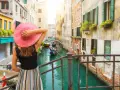 Una donna con cappello rosa ammira un canale veneziano con gondole. Un assaggio di cosa vedere a Venezia in un giorno.