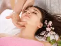 A woman receives an anti aging facial massage, her eyes closed in relaxation. Delicate pink berries adorn her dark hair.