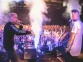 Krzysztof, w wieku swoich najlepszych lat, na scenie z mikrofonem, tłum szaleje, dym i światła tworzą atmosferę koncertu.