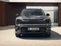 Szary SUV Kia EV5 z charakterystycznymi światłami LED, zaparkowany przed nowoczesnym budynkiem.