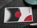 Tarjeta de presentación con diseño moderno en blanco, negro y rojo. Se aprecian círculos y puntos, con una regla y cúter cerca, sugiriendo la creación de distintos tamaños DIN.