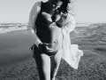 Donna incinta si gode il sole in spiaggia, accarezzando il pancione. La brezza marina le scompiglia i capelli.