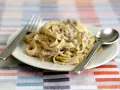 Un piatto di tagliatelle ai funghi cremose, con forchetta e cucchiaio pronti per gustare questo delizioso primo.