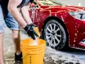 Ręce w czarnych rękawiczkach płuczą gąbkę w żółtym wiadrze, przygotowując się do mycia auta na dwa wiadra.