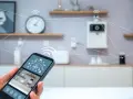 A hand holds a smartphone displaying an IoT interface, showing how you can control an IoT connected smart device remotely.