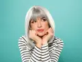 Donna con eleganti capelli grigi, appoggiata alle mani, con un'espressione sognante.