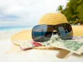 Sonnenbrille, Hut und Geld am Strand. Der Spiegel der Brille zeigt eine Person, die den Urlaub genießt. Ein Symbol für den **Urlaubsgeldanspruch**.