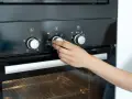 Hand dreht Temperaturregler am Ofen auf 250 Grad. Die Frage "wie lange Ofen vorheizen" wird durch das Einstellen der Temperatur beantwortet.