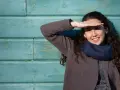Ragazza sorride, coprendosi gli occhi dal sole. Il fastidio alla luce non le impedisce di godersi la giornata.