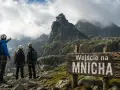 Trzech turystów w kaskach i z plecakami stoi przed znakiem "Wejście na Mnicha" w Tatrach.
