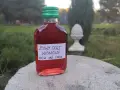 Butelka żywego octu wiśniowego, 100 ml, z zieloną zakrętką. W tle ogród. Ocet wiśniowy właściwości zdrowotne.