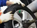 Tecnico con guanti esegue equilibratura gomme per eliminare vibrazioni. Ruota su macchinario specifico.