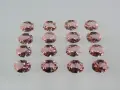 Sedici pietre di morganite ovali, rosa pesca, disposte in file ordinate. Le loro sfaccettature riflettono la luce, mostrando le belle morganite proprietà.