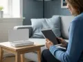 Kvinna med surfplatta bredvid en vit router som visar statuslampor. Hon kanske justerar wifi frekvens för bättre täckning.