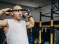 Man med rakad skalle utför face pulls med ett rep i ett gym.