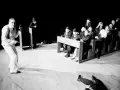 Na scenie mężczyzna przemawia do siedzących w ławkach ludzi. Na podłodze leży martwa postać. Umarła klasa.