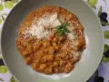 Pyszny makaron z ciecierzycy w sosie pomidorowym, posypany parmezanem i udekorowany gałązką rozmarynu.