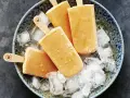 Vier selbstgemachte Papaya-Eis am Stiel liegen auf zerstoßenem Eis in einer blauen Schale.