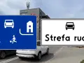 Dwa znaki drogowe: niebieski z piktogramami pieszych, dzieci bawiących się piłką i samochodu, oraz biały z napisem "Strefa ruchu" i ikoną samochodu.