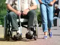 Osoba na wózku inwalidzkim z laską, obok niej idzie osoba w jeansach.