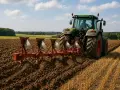 Zielony traktor z pługiem orze pole. Jaki pług do ciągnika 75km? Ten czteroskibowy radzi sobie świetnie.