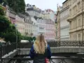 A woman with blonde hair gazes at colorful buildings, perhaps planning her day trips from Prague by train.