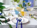 Festligt dukat bord med champagneglas, blå och gula band som knyts i en blå rosett, samt en studentmössa.