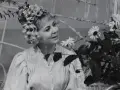 Ilona Stawińska w kwiecistej fryzurze i jasnej sukni, otoczona kwiatami, wygląda jak z baśni.