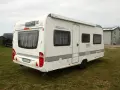 Biała przyczepa kempingowa Caravelair 495 RE na trawie, z widocznym logo MANCZAK.PL.