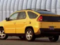 Żółty Pontiac Aztek z charakterystycznym tyłem i spojlerem, zaparkowany przed falistą, metalową ścianą.