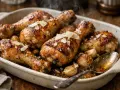 Délicieux pilons de poulet rôtis, parsemés de copeaux de parmesan et accompagnés d'ail confit, fumant dans un plat en céramique.