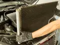 Mechanik w rękawicach wyjmuje chłodnicę klimatyzacji z silnika samochodu.