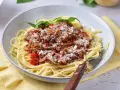 Pyszne spaghetti z bogatym sosem mięsnym na bazie passaty, posypane parmezanem i udekorowane listkami bazylii.
