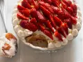 Delizioso tiramisù alle fragole, guarnito con panna montata, fragole fresche e pistacchi. Una fetta servita su un cucchiaio.