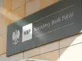 Tablica z godłem Polski i napisem "NBP Narodowy Bank Polski". Decyzje NBP wpływają na obniżkę stopy procentowej.