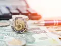 Złota moneta 5 złotych na stosie monet i banknotów. Obok długopis i kalkulator, sugerujące planowanie finansowe i możliwość recoverso rmc.