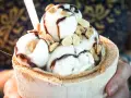 Cremiges Pina Colada Eis in einer Kokosnussschale, beträufelt mit Schokoladensauce und garniert mit Nüssen. Ein tropischer Genuss!