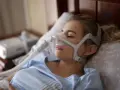 Kobieta śpi w masce CPAP, która pomaga w leczeniu bezdechu sennego. Urządzenie zapewnia ciągłe doprowadzanie powietrza, łagodząc objawy.