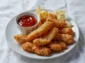 Chrupiący kurczak w panierce, podany z ketchupem i chipsami. Idealna przekąska na imprezę.