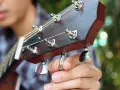 Nahaufnahme: Eine Hand stimmt eine 12-saitige Gitarre. Die Saiten sind gespannt, die Mechaniken glänzen.