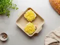Dwa tosty z serem i beszamelem, przygotowane do zapieczenia jako croque madame. Obok gałka muszkatołowa i świeże zioła.
