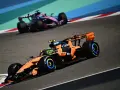 Un coche de Fórmula 1 naranja y negro compite en la pista, anticipando el reglamento F1 2026. Otro coche rosa y azul le sigue de cerca.