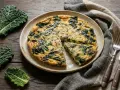 Frittata con cavolo nero, un piatto rustico e saporito, pronto per essere gustato. Accanto, foglie fresche di cavolo nero e posate d'argento.