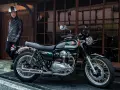 Mężczyzna w skórzanej kurtce i kasku stoi obok klasycznego motocykla Kawasaki W800 w kolorze ciemnozielonym.