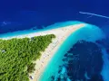 Rajskie chorwackie plaże z turkusową wodą i zielonym lasem sosnowym. W oddali widać łódź motorową.
