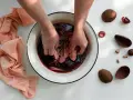 Mani che tingono tessuti in una bacinella con liquido scuro, circondata da bucce di avocado. Un processo naturale per come tingere i tessuti.