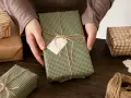 Oto jak zapakować bilety na prezent: ręce owijają zielono-brązowy prezent sznurkiem, dodając pustą metkę.
