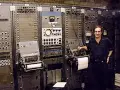 Mann steht neben einem riesigen, frühen Computer, dem ersten Synthesizer der Musikgeschichte.