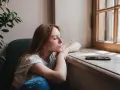 Zamyślona rudowłosa dziewczyna siedzi przy oknie, zastanawiając się, **benching co to** znaczy. Obok leży telefon.