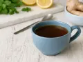 Une tasse de tisane pour mal de gorge, avec du gingembre, du citron et de la menthe à proximité.